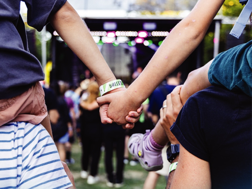 Doi adulți ținându-se de mână, cu copiii pe umeri, în fața scenei la Guitar Meeting Festival